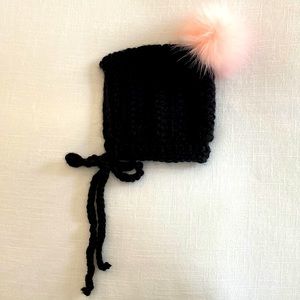 Black crocheted baby bonnet with light pink faux fur pom